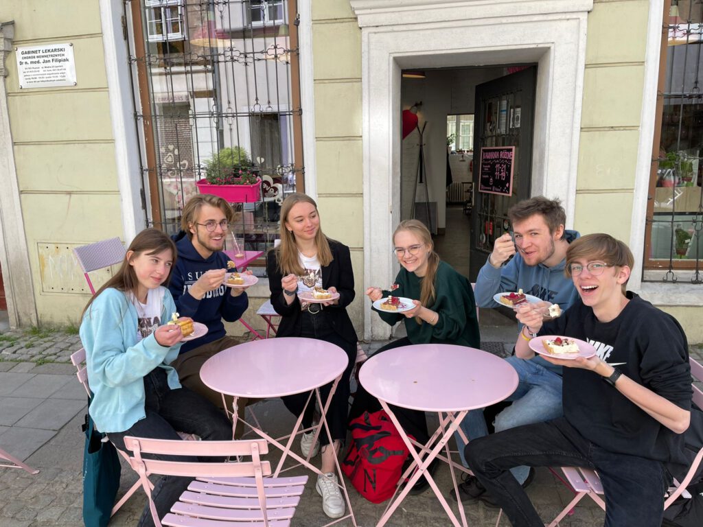 Zdjęcie grupowe przed kawiarnią, na którym wszyscy uczniowie jedzą ciasto. 